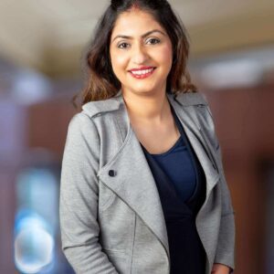 A woman with layered hair is smiling at the camera while wearing a gray blazer using different background
